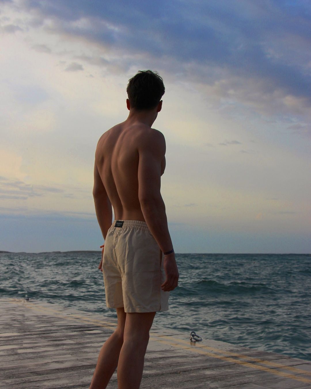 jeune homme de dos musclé regardant la mer en short de bain recyclé pour homme beige crème