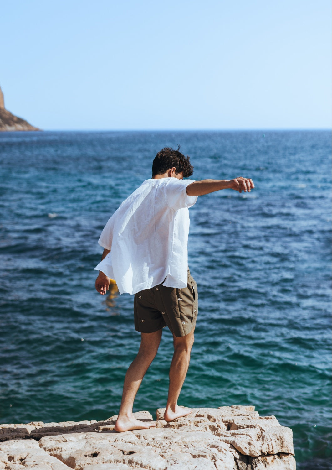 caleçon de bain homme vert kaki sur homme face à la mer, au vent avec une chemise en lin blanche