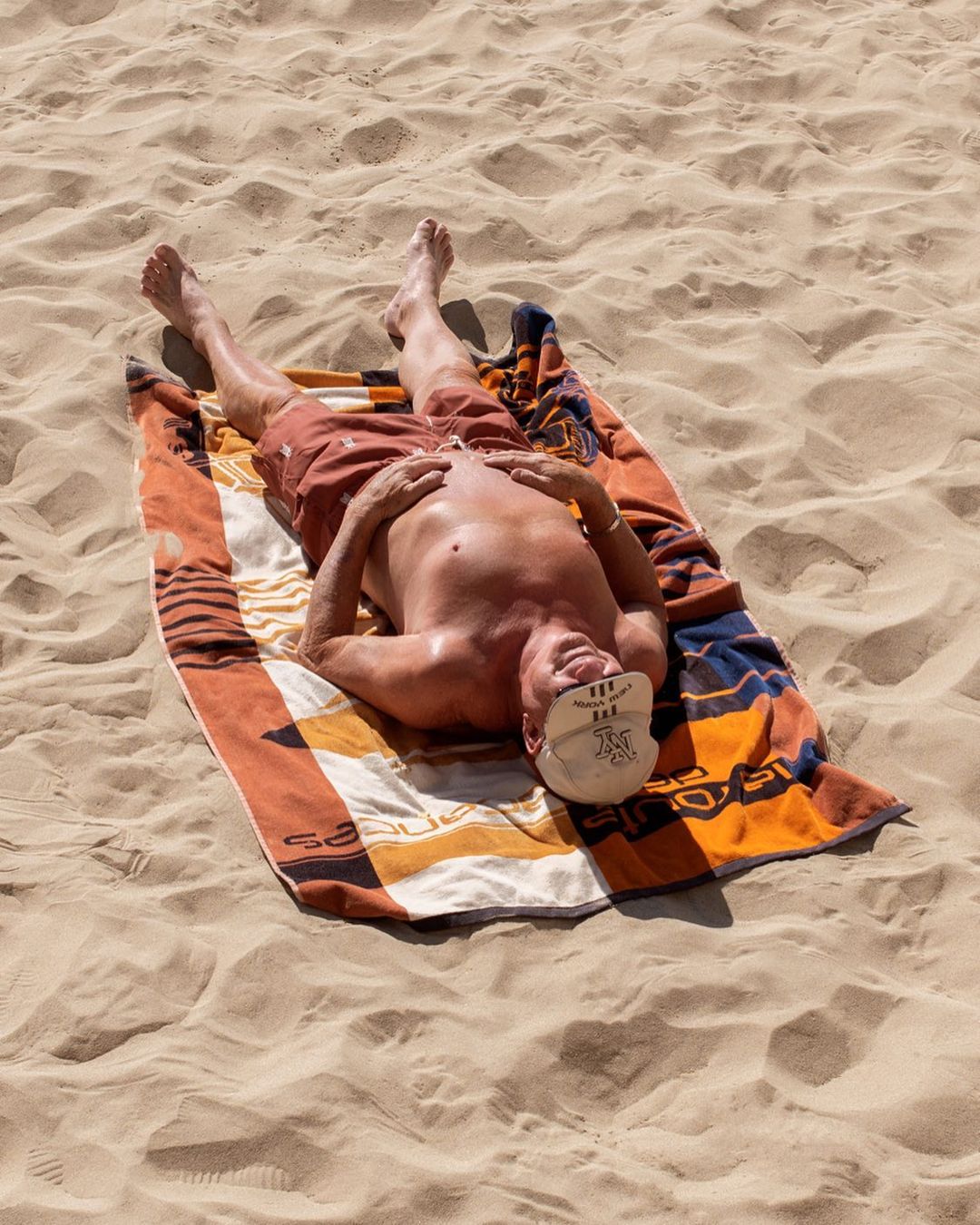senior allongé sur la plage avec un short de bain homme rouge terracotta recyclé à Marseille