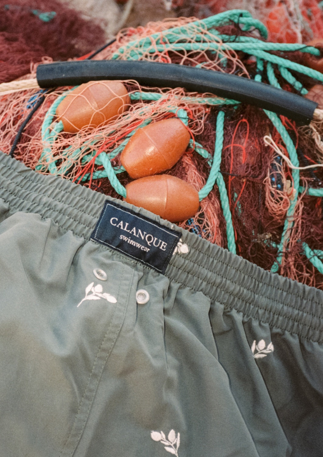 maillot de bain masculin recyclé vert posé sur des filets de pêche usagés