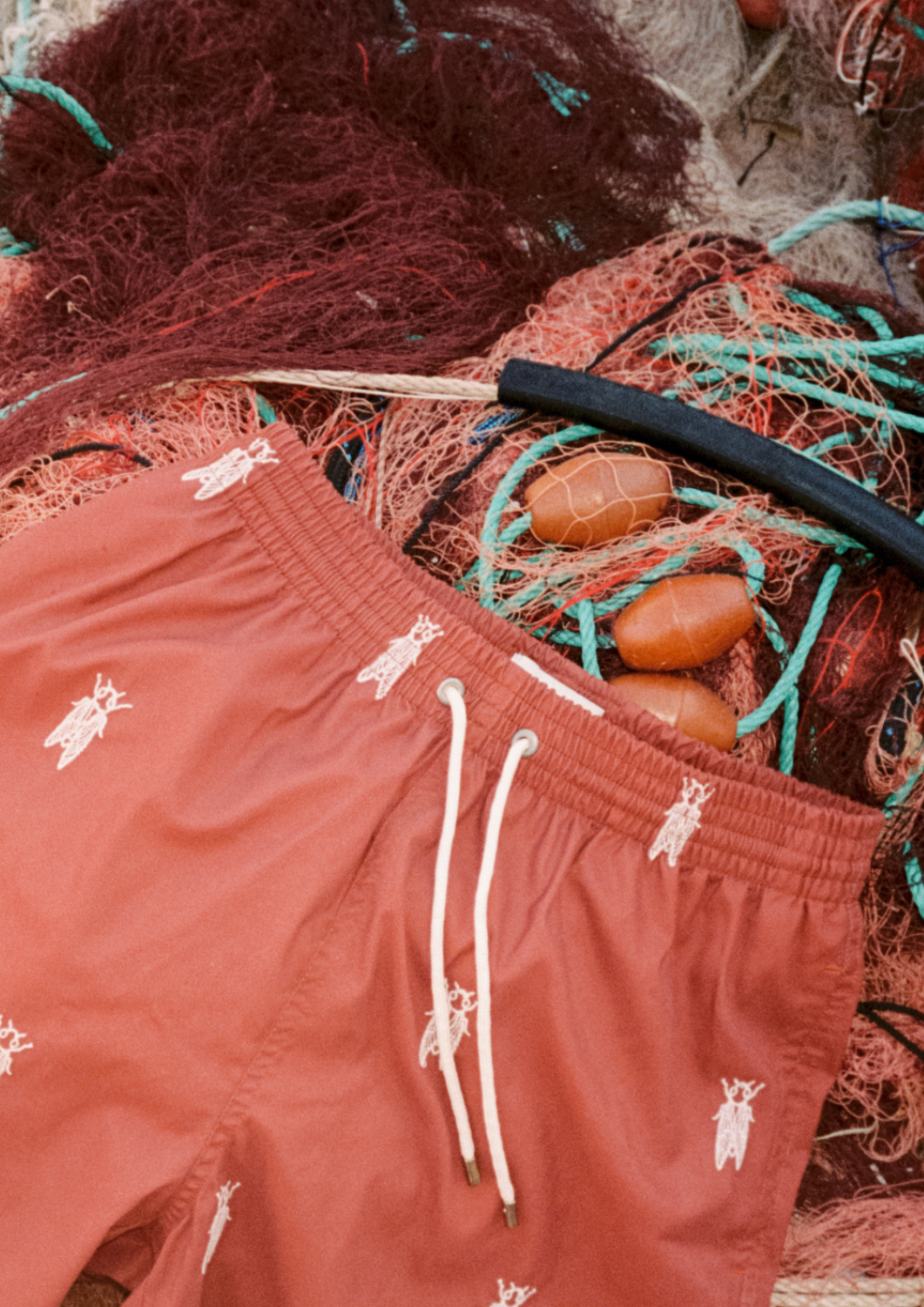 un short de plage terracotta recyclé est posé sur des filets de pêche dans un port